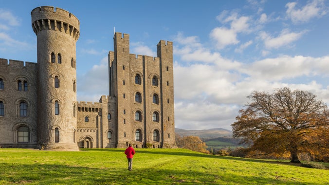 Visitor walking in the grounds of Penrhyn Castle in autumn, with castle and hills in the background in Gwynedd, Wales.